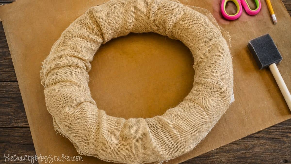 Foam wreath form wrapped in burlap fabric, ready for decorating as the base of a DIY popcorn kernel fall wreath.