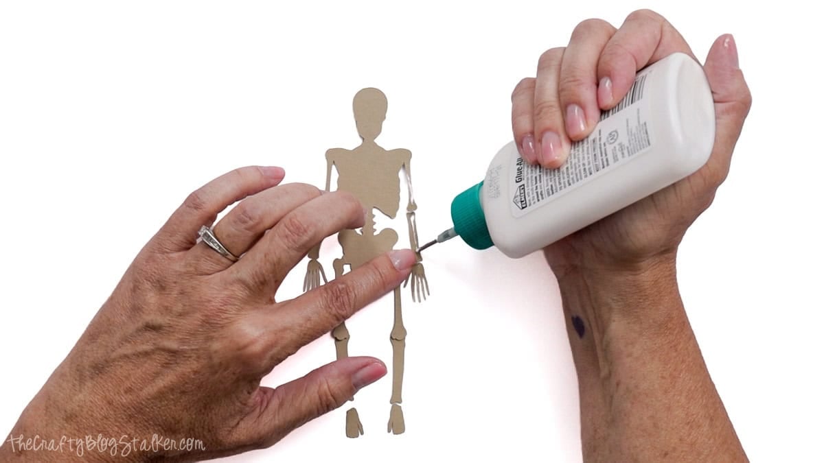 Glue is applied to the arm joint of a kraft paper skeleton while assembling a posable Halloween skeleton craft.