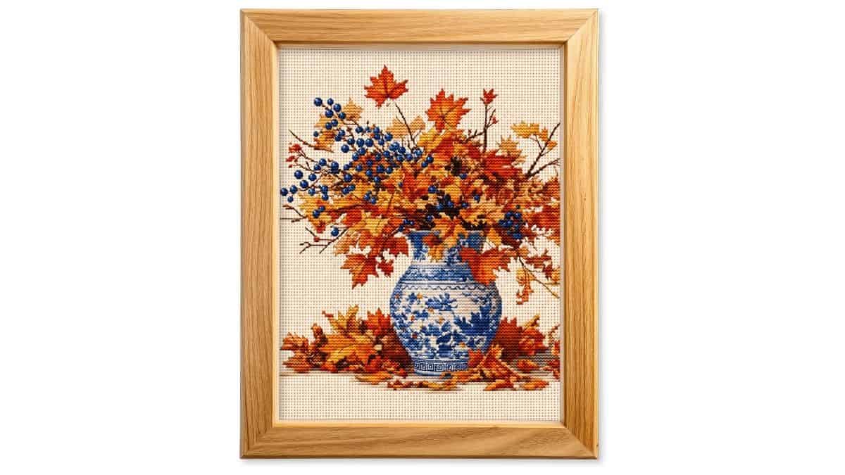 Framed preview of a printable cross stitch design featuring a blue and white vase filled with colorful autumn leaves and blue berries.