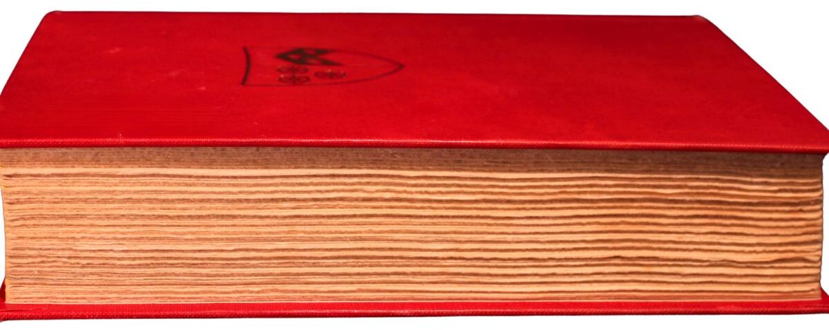 A red hardcover book viewed from the side, showing its thick, unevenly cut pages and a subtle crest design on the cover.