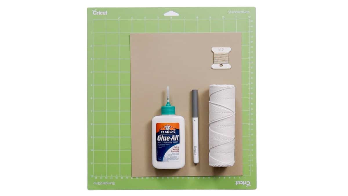 Supplies for a Cricut skeleton banner include kraft paper, glue, a Cricut pen, white cord, twine, and a StandardGrip cutting mat.