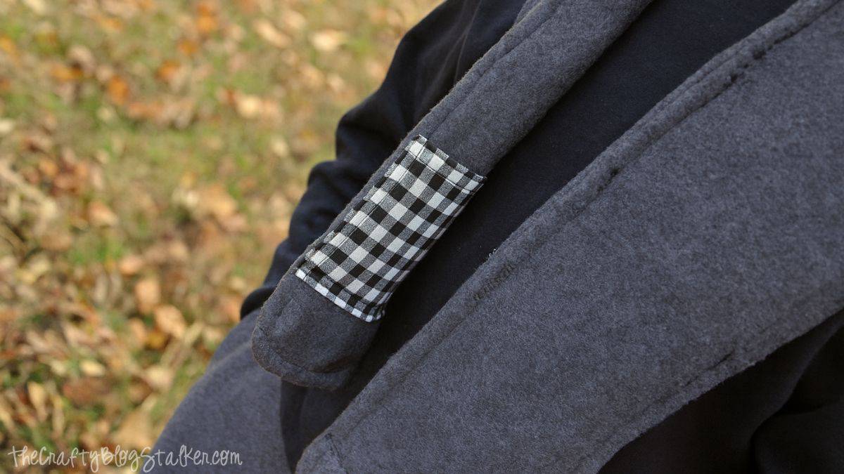 A child wearing a gray fleece scarf that features a small black-and-white checkered pocket sewn onto the side.