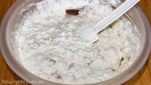 Creamy cottage cheese clam dip mixed in a large bowl with visible minced clams and a white rubber spatula.