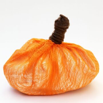 DIY pumpkin made with orange-dyed cheesecloth and a brown wrapped stem, displayed against a plain white background.