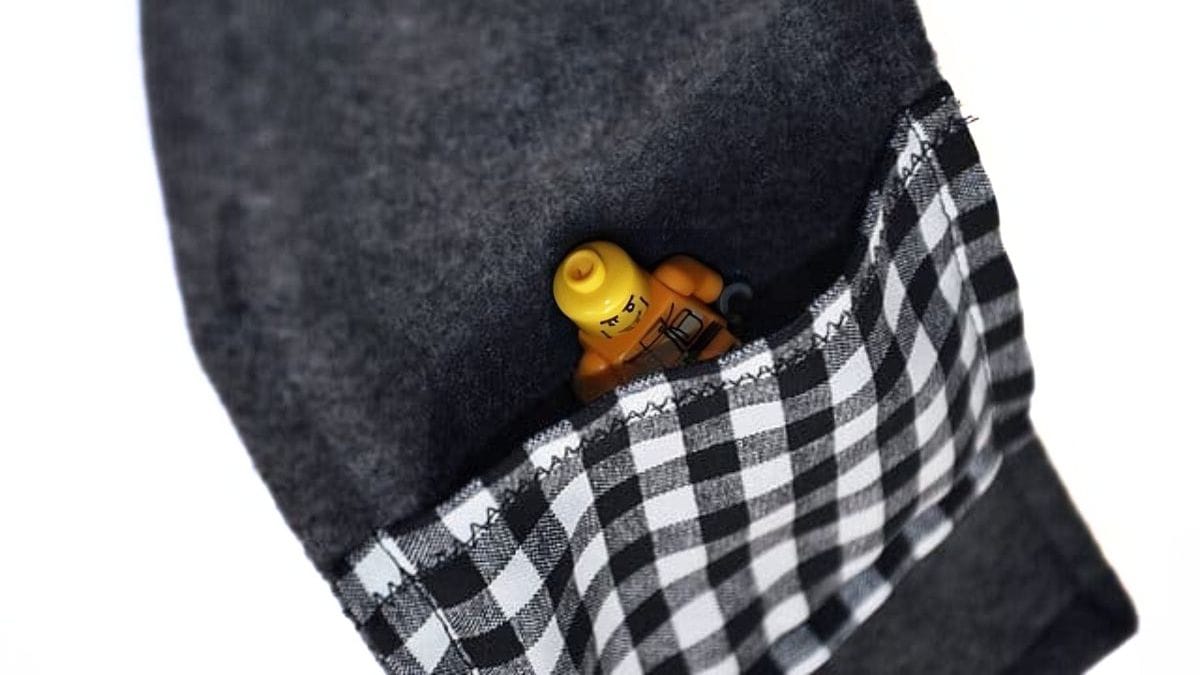 A gray fleece scarf with a black-and-white checkered pocket holding a small LEGO minifigure partially tucked inside.