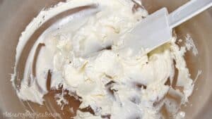 Cream cheese softened in a microwave-safe bowl with a white spatula for making creamy cottage cheese clam dip.
