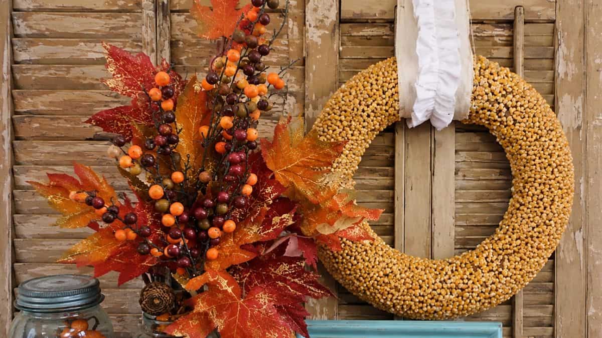 Autumn Popcorn Wreath Tutorial DIY popcorn kernel wreath displayed with colorful fall leaves and berry stems on rustic wood shutters, creating a warm autumn farmhouse decoration.