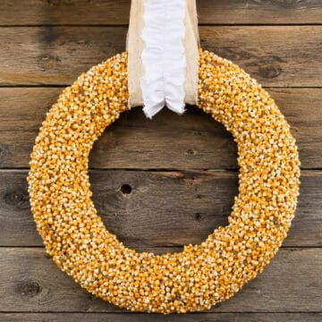 DIY popcorn kernel wreath hanging on a rustic wood wall with a cream fabric and ruffled white ribbon for simple fall farmhouse decor.