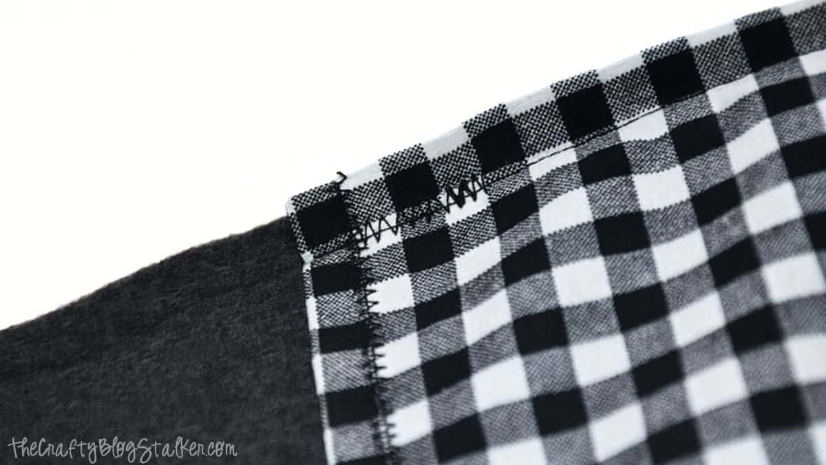 A close-up view of a fleece scarf with a black-and-white checkered pocket, showing zigzag stitching securing the pocket to the scarf.