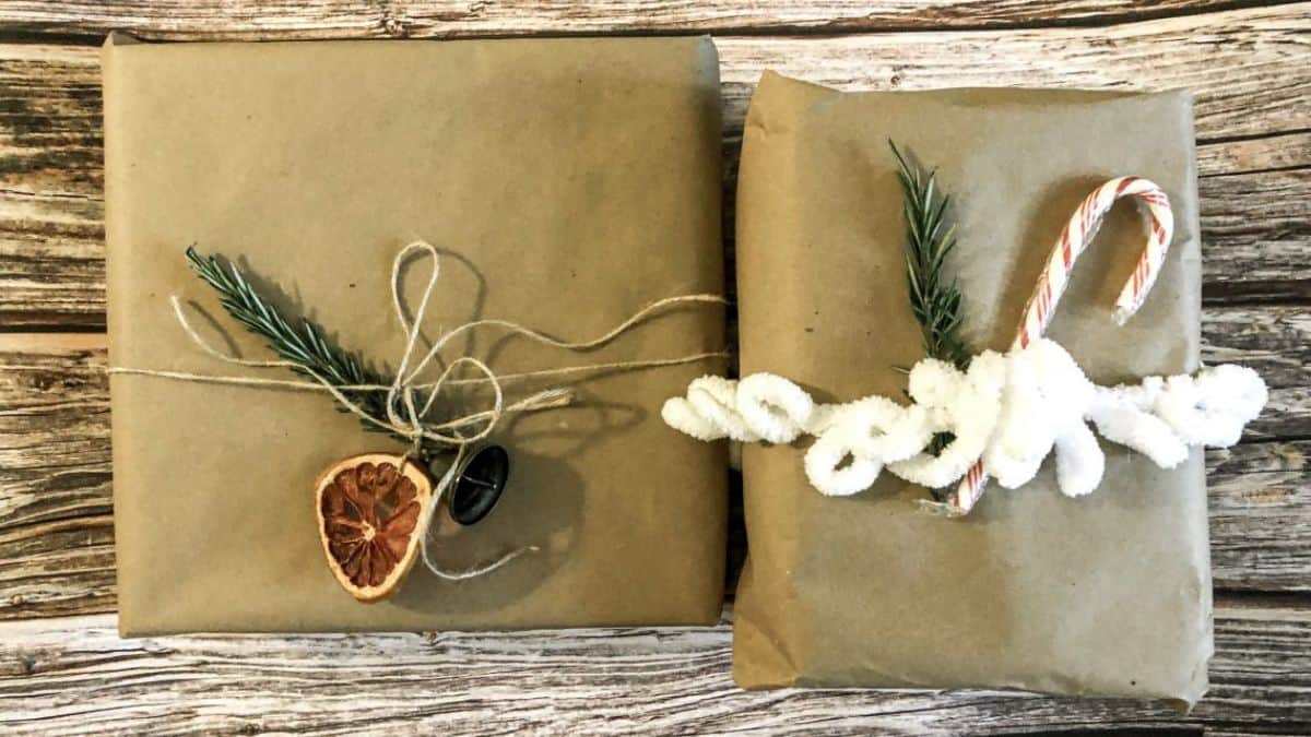 Two Christmas gifts wrapped in kraft paper and decorated with twine, greenery, dried citrus, a candy cane, and white yarn.