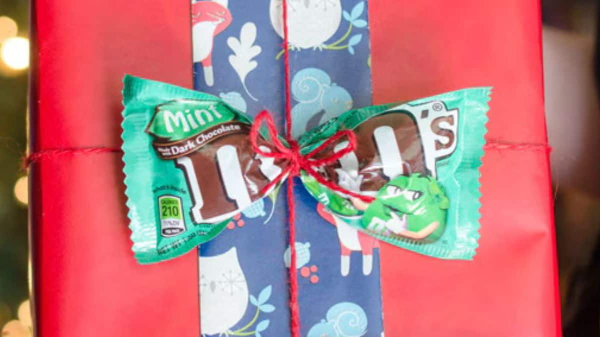 Red wrapped gift decorated with patterned paper, red string, and two mint M&M's candy packages tied in a bow.