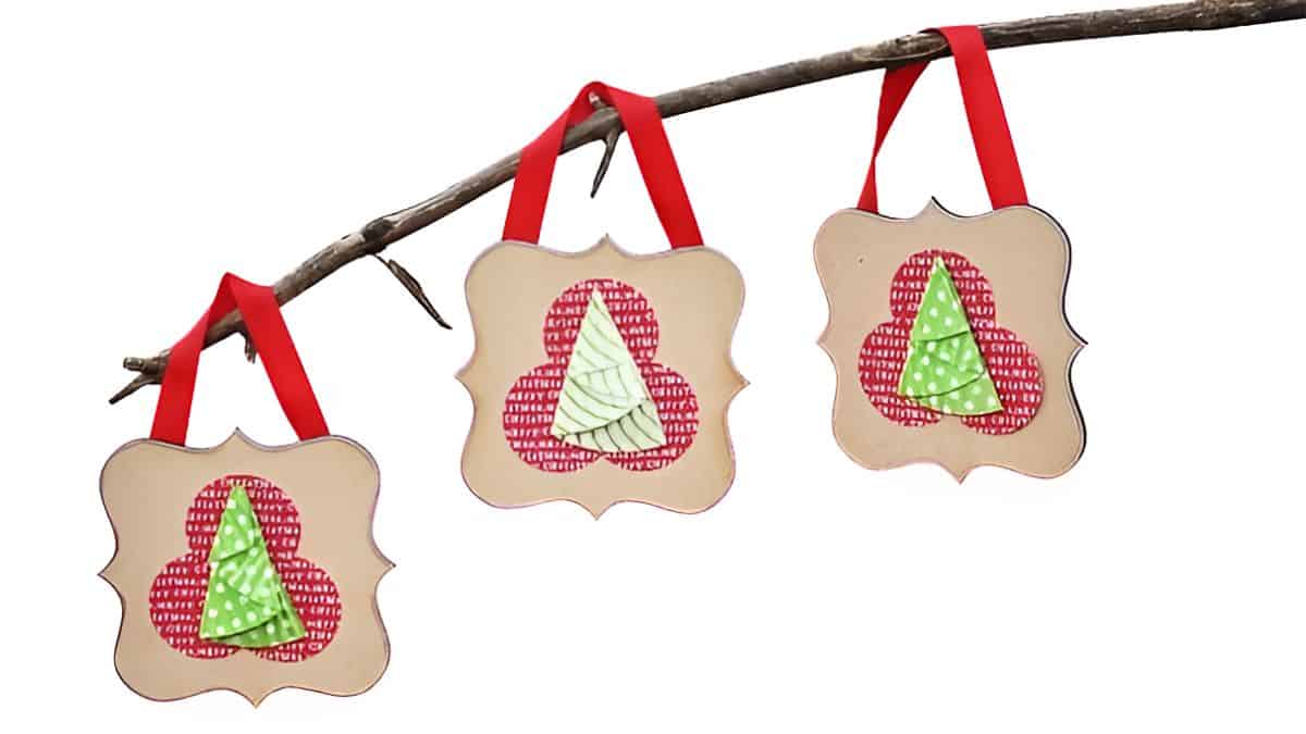 DIY Christmas ornaments made from layered cupcake liners shaped into trees, each hung with a red ribbon on a branch.