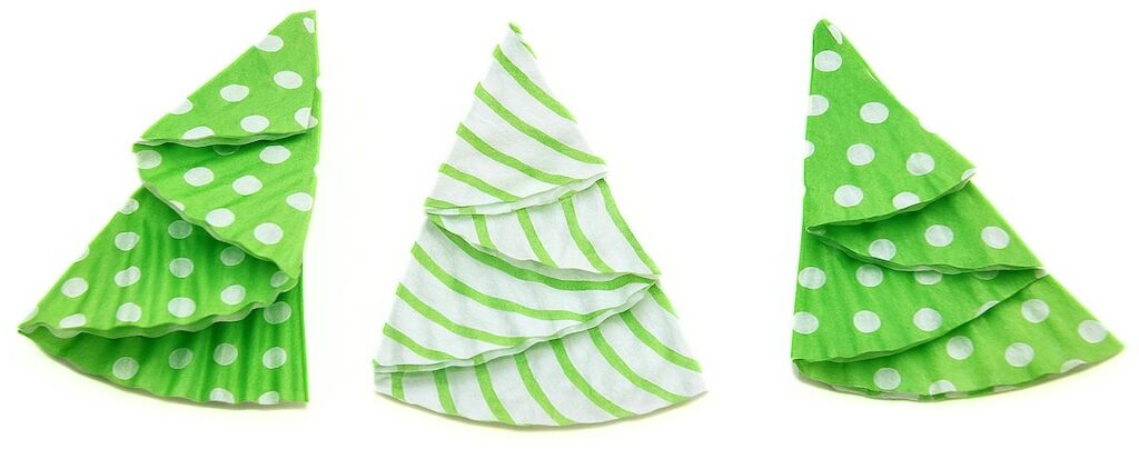 Three folded cupcake liners shaped into layered Christmas trees, shown in green patterns and arranged side by side on a white background.