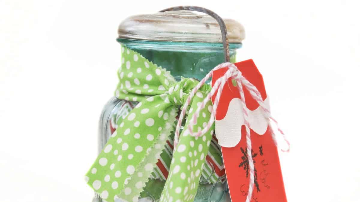 Vintage blue mason jar decorated with a green polka-dot fabric bow and a red holiday gift tag tied with twine.