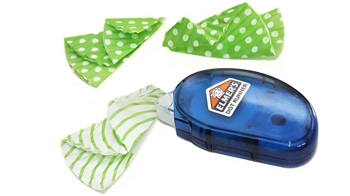 Folded green cupcake liners shaped into small tree pieces with an Elmer's dot runner glue tool placed beside them on a white background.