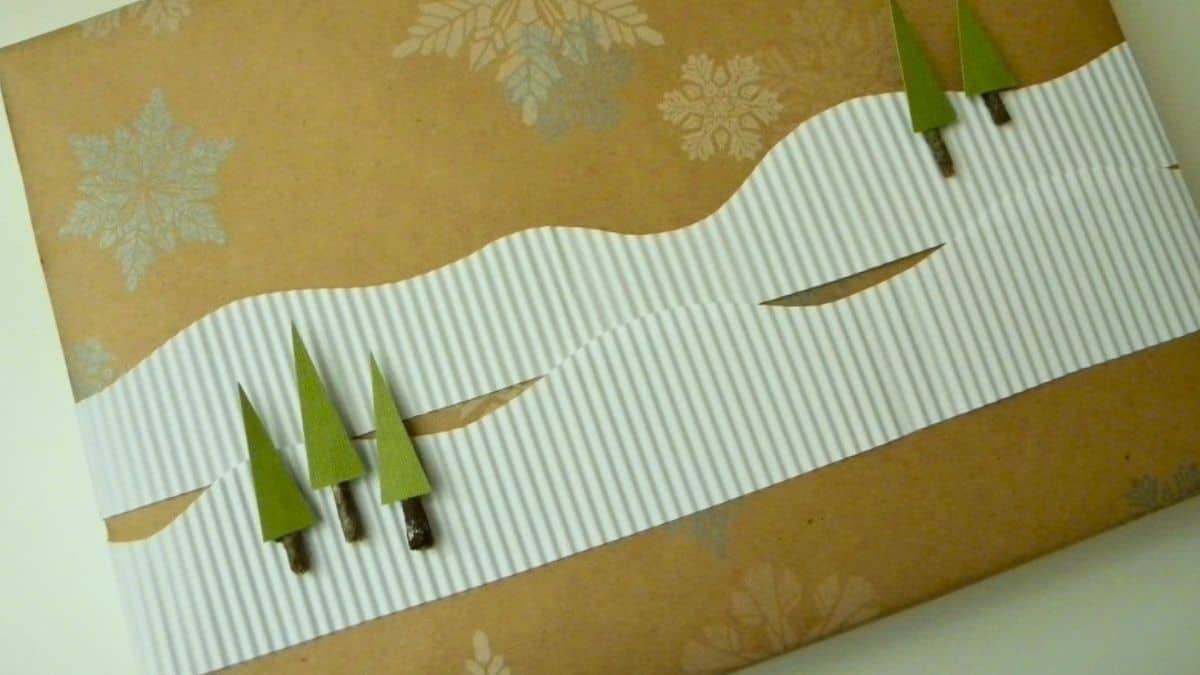 Handmade gift wrap with kraft paper, white corrugated paper, stamped snowflakes, and small green paper trees.