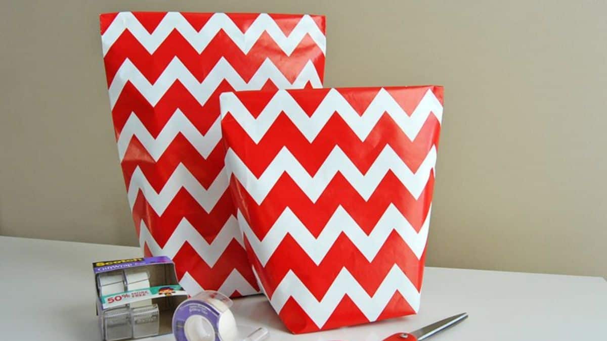 Two handmade gift bags made from red and white chevron wrapping paper with tape and scissors on the table.