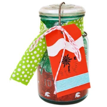 Vintage mason jar decorated with a green polka dot fabric bow and a handmade red gift tag wrapped in twine and yarn, used as a festive gift card holder.
