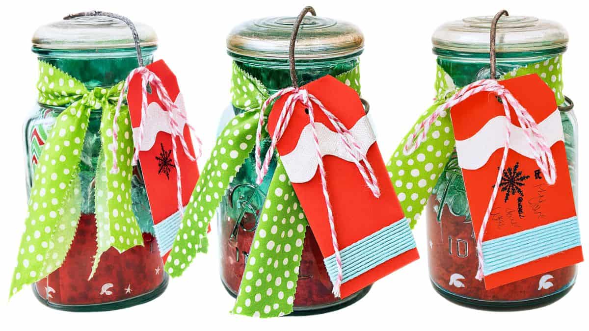 Three mason jar gifts decorated with green polka dot fabric, twine, and red handmade tags wrapped around the jars.