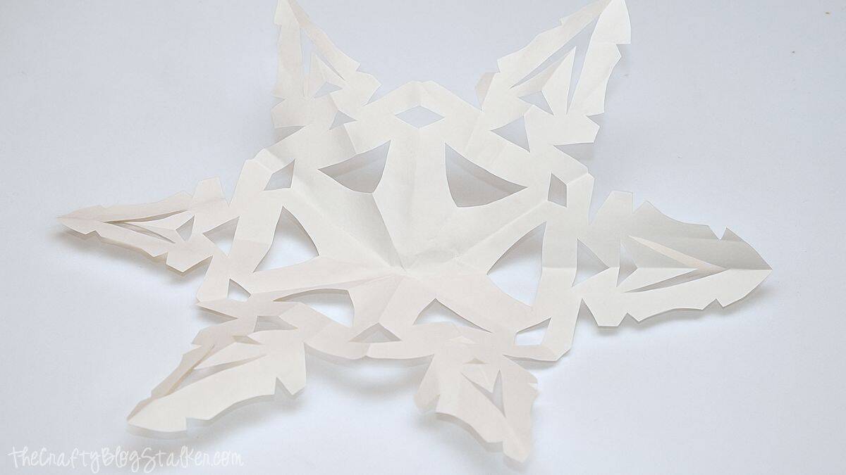 A white paper snowflake with intricate cutout details displayed on a light surface, ready to be used for a holiday craft or decoration.