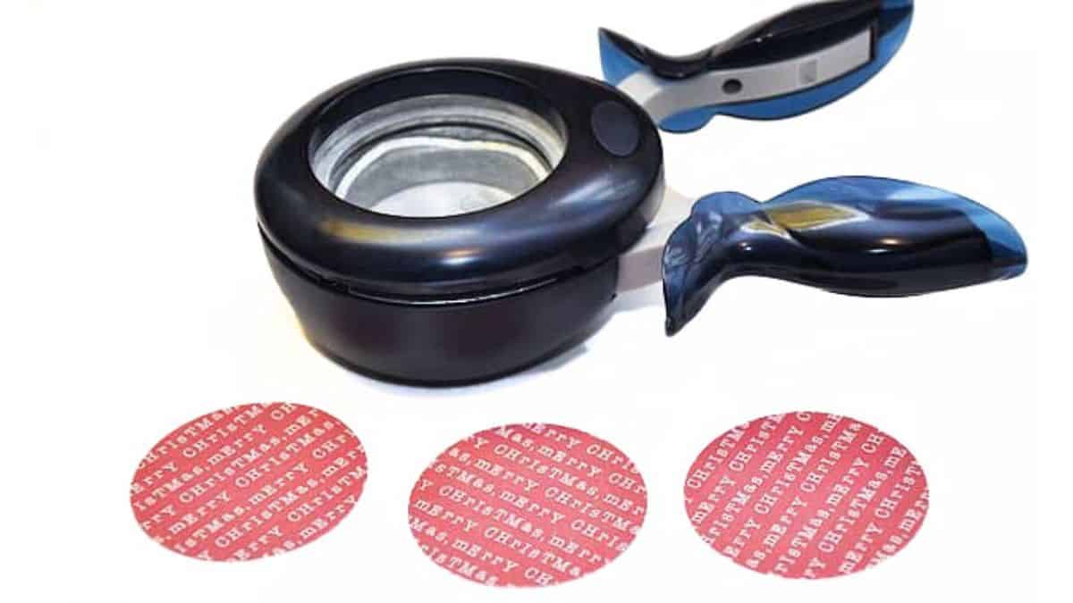 A handheld circle paper punch with three punched red patterned paper circles displayed in front of it.