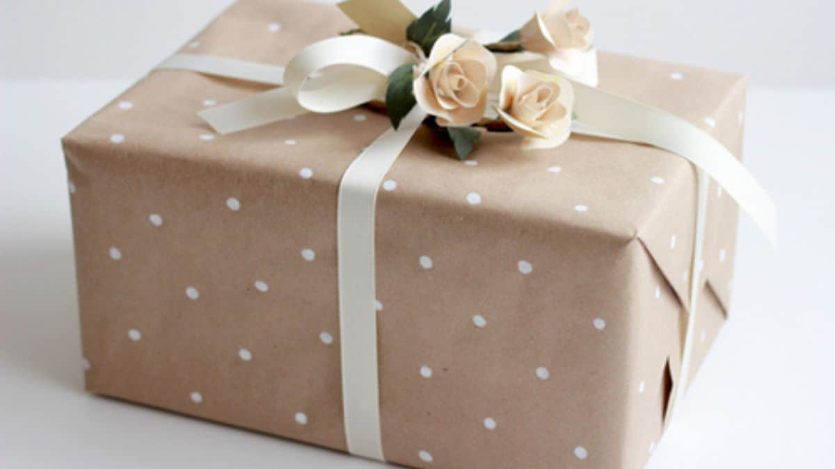Gift wrapped in kraft paper with white polka dots, cream ribbon, and small paper roses with green leaves.