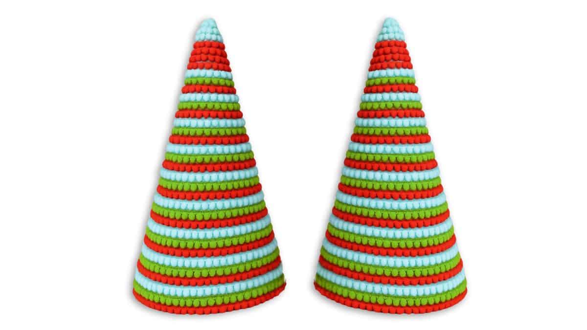 Two cone-shaped Christmas trees decorated with red, green, and light blue pom pom trim in horizontal stripes on a white background.