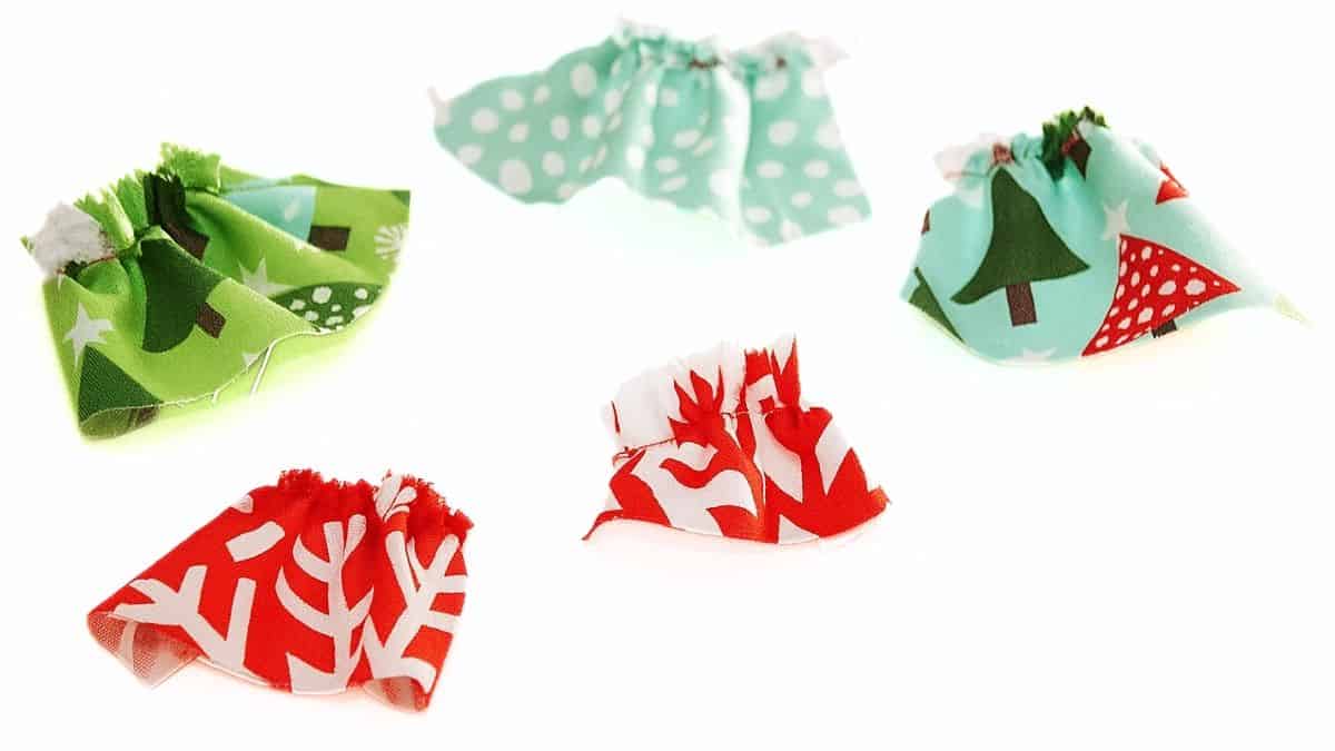 Five small ruffled fabric pieces in red, green, and aqua Christmas prints arranged on a white background for a holiday craft project.