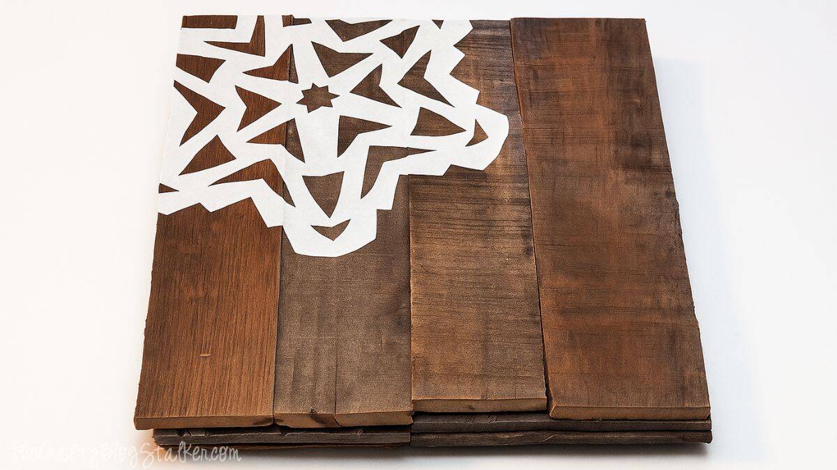 Stack of rustic wooden boards with a white paper snowflake Mod Podged onto the top board, creating a handmade holiday table decoration.