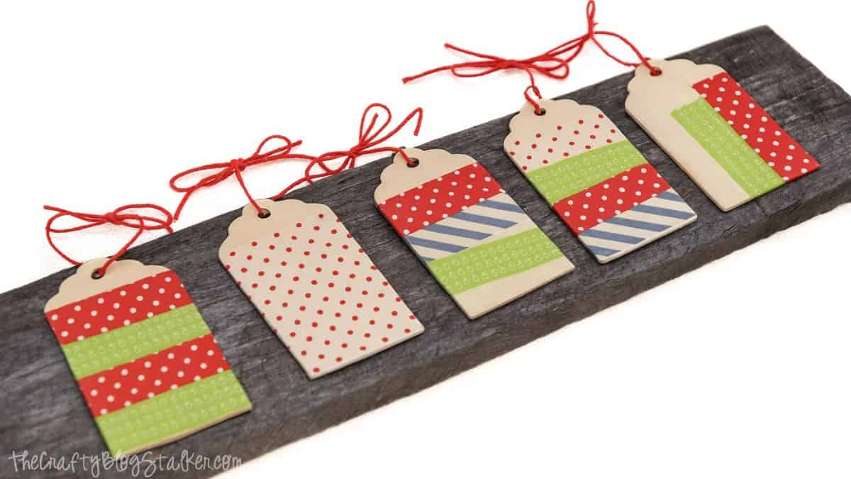 Washi Tape Ornaments made with wooden tags Five handmade wooden gift tags decorated with patterned washi tape and tied with red string, arranged in a row on a rustic board.