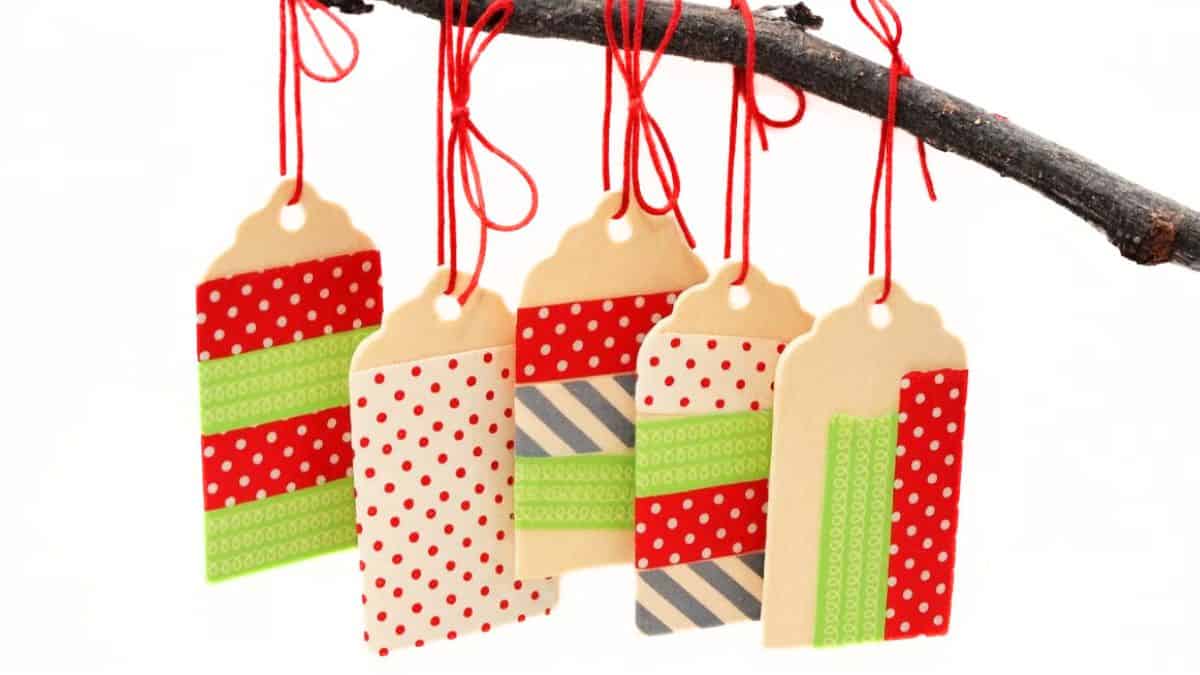 Washi Tape Ornaments made with wooden tags Five wooden tags decorated with colorful washi tape and hung from a branch with red string, creating simple handmade ornaments.