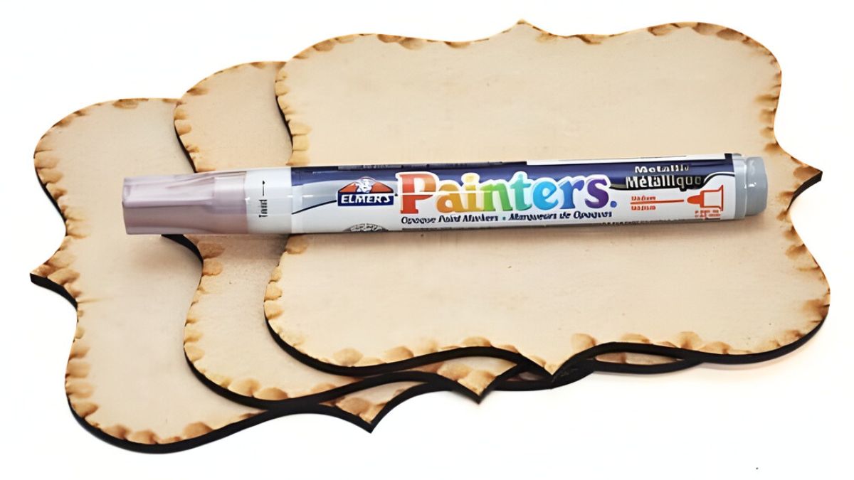 Three unfinished wood plaque shapes stacked together with a metallic paint marker resting on top.