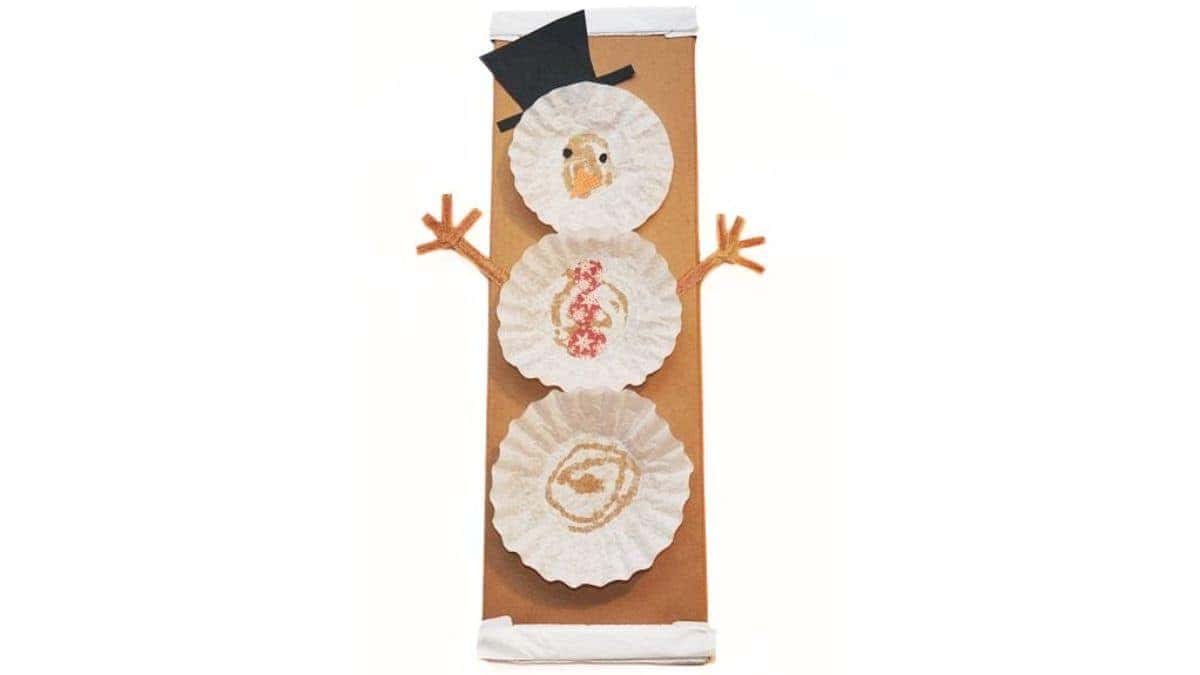DIY Coffee Filter Snowman - A fun Craft for kids via cherishedblsis.com Finished coffee filter snowman craft made with stacked coffee filters, paper hat and nose, and pipe cleaner arms, attached to a brown paper gift bag.