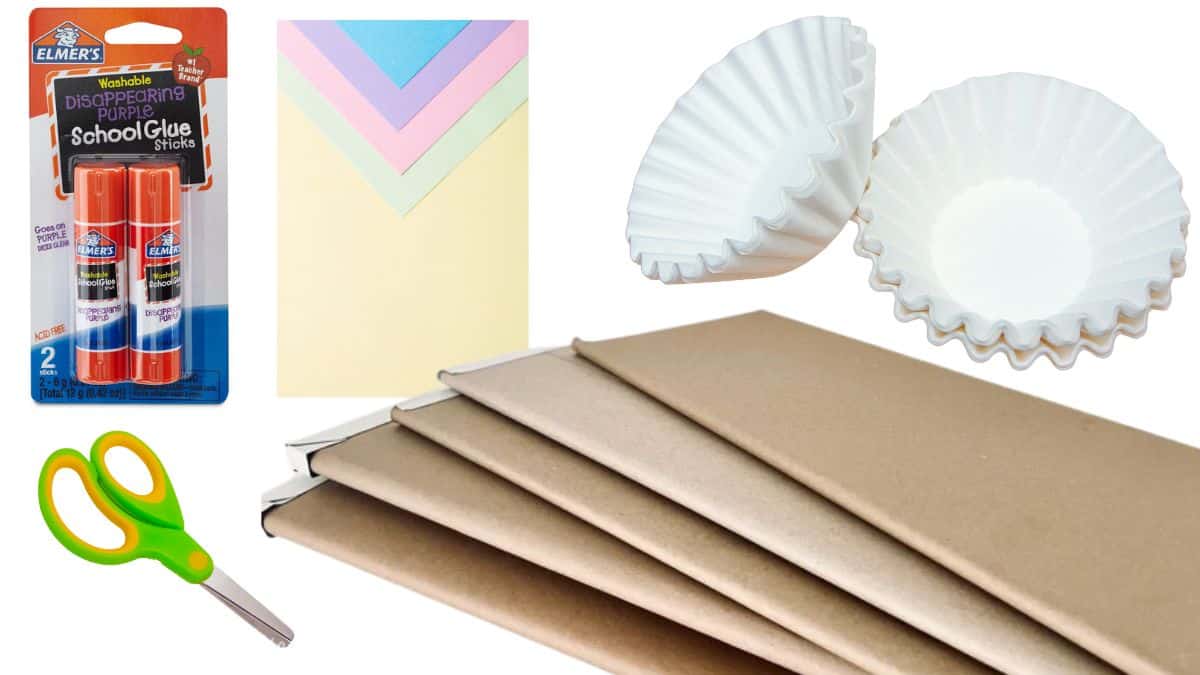 Craft supplies for a coffee filter snowman project, including glue sticks, pastel paper, coffee filters, scissors, and brown paper bags.