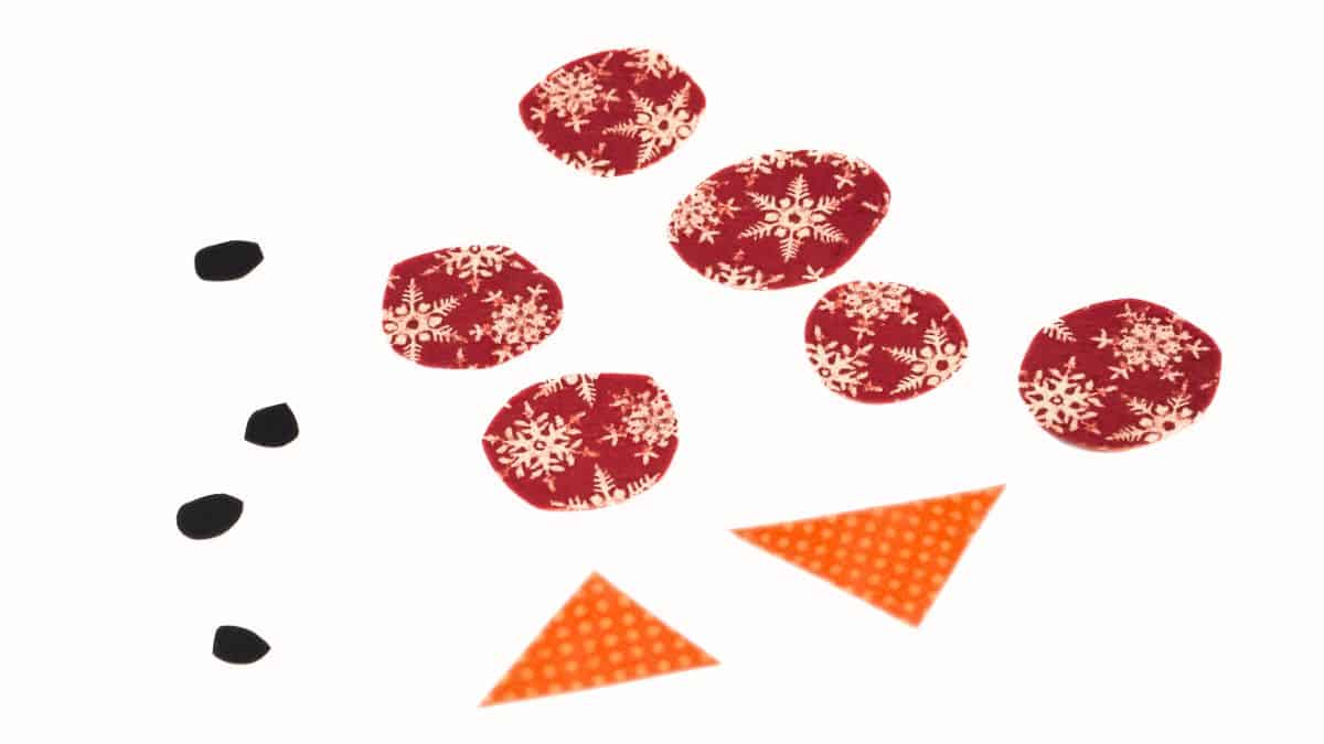 DIY Coffee Filter Snowman - A fun Craft for kids via cherishedblsis.com Cut paper pieces for a snowman craft, including small black shapes for eyes and mouth, patterned circles for buttons, and triangle shapes for carrot noses.