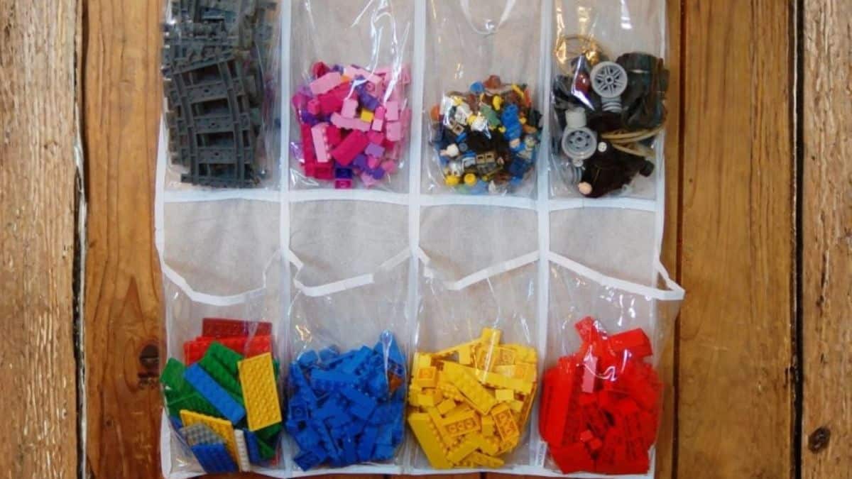 Clear hanging organizer with multiple pockets filled with LEGO pieces sorted by type and shape, mounted on a wooden surface for easy storage and access.