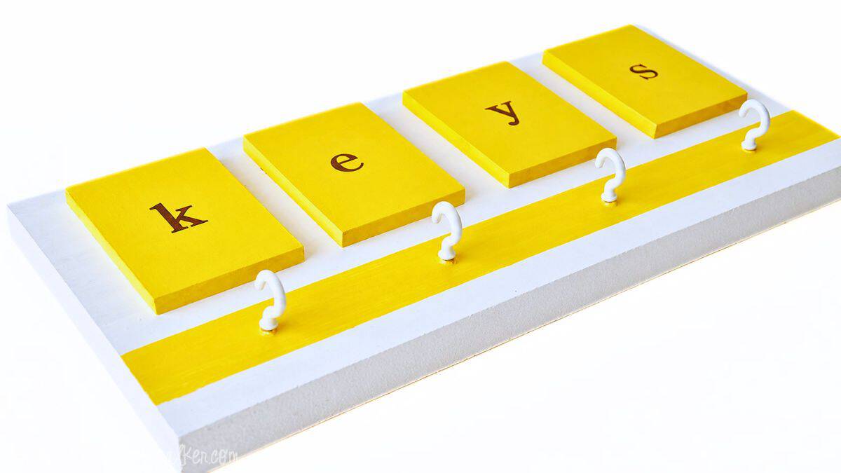 Diagonal view of a yellow and white DIY key holder with tiles spelling 