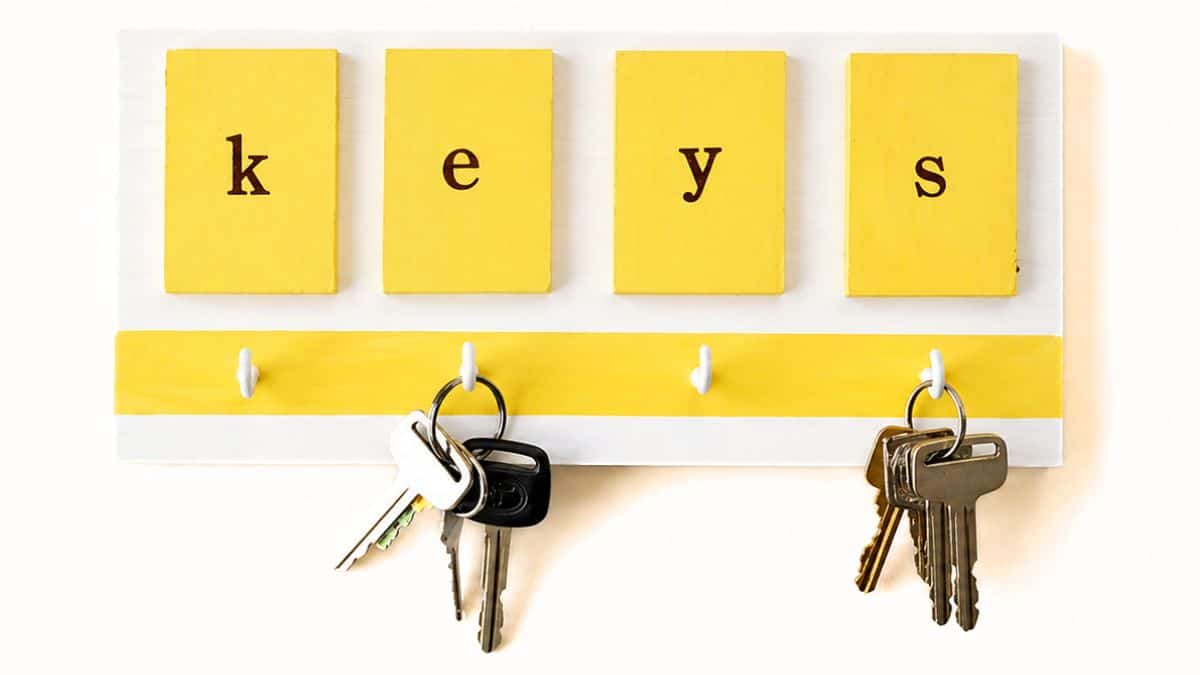 Yellow wall-mounted key holder with four hooks and tiles spelling 