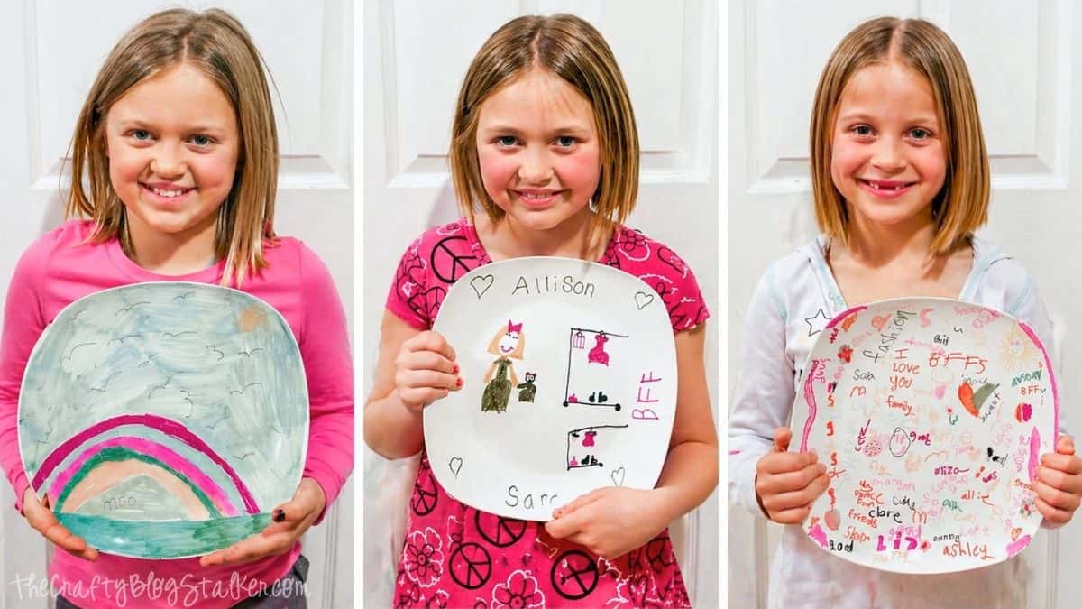 Three girls each holding a decorated ceramic plate with colorful drawings and names, showing DIY Sharpie plate designs.