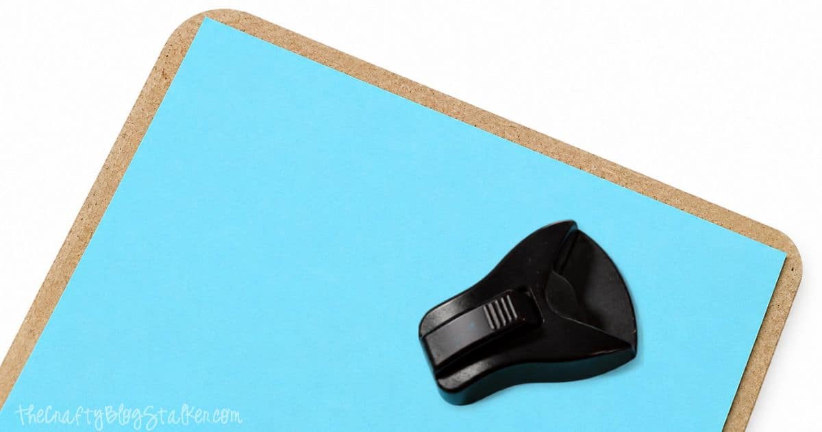 Corner rounder punch trimming the corner of blue paper on a standing clipboard backing to create smooth, rounded edges.