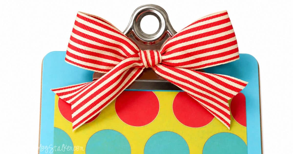 Close-up of a decorative standing clipboard with colorful polka dot paper and a red-and-white striped ribbon bow attached to the metal clip.