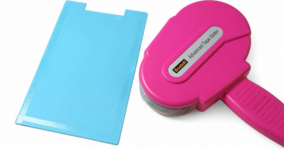 Blue paper with double-sided adhesive applied around the edges beside a pink tape runner, ready to attach to a decorative standing clipboard.