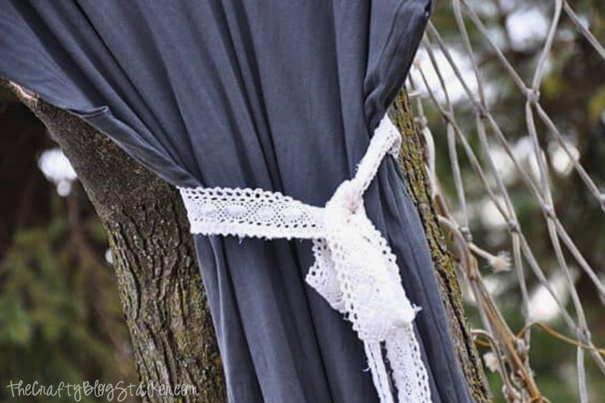 Close-up of a dark gray maternity dress tied with a white lace sash, wrapped around the waist and knotted at the side, shown hanging against a tree.