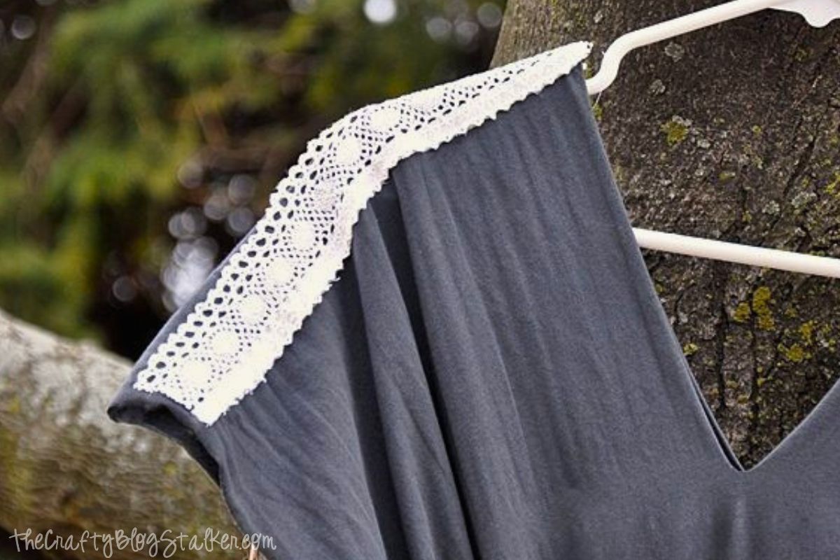 Close-up of a dark gray maternity maxi dress on a hanger, highlighting a decorative white lace trim sewn along the edge of the short sleeve.
