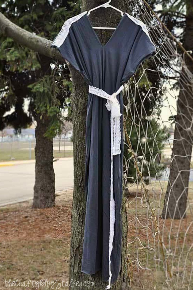 Dark gray maternity maxi dress with white lace trim on sleeves and matching waist tie, hanging on a tree branch with a park-like background.