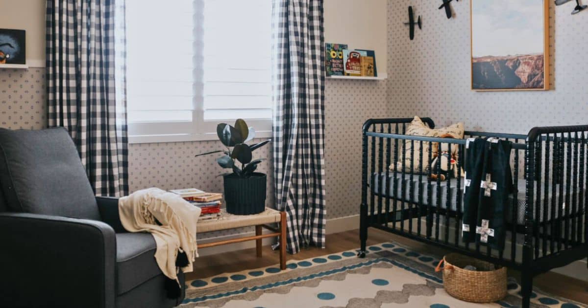 Modern baby boy nursery with a black crib, gray glider, blue plaid curtains, airplane decor, and a patterned rug in a cozy, neutral space.
