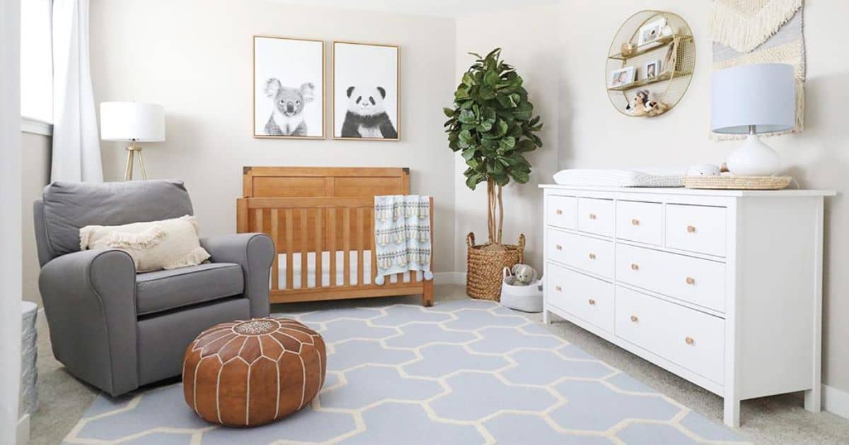 Neutral nursery with a wood crib, gray glider, white dresser, animal wall art, indoor tree, and a gray geometric rug in a bright, modern room.