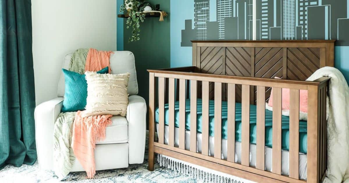 12 Beautiful Boy Nursery Ideas Modern gender-neutral nursery with a wood crib, white glider chair, teal and coral accents, dark curtains, and a city skyline mural behind the crib.
