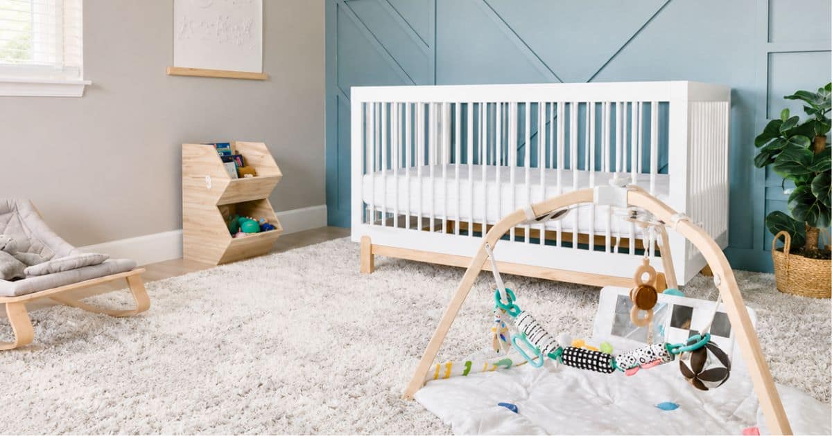 Modern nursery with a white crib, blue accent wall, wooden play gym, plush rug, toy storage, and minimalist decor in soft blue and neutral tones.