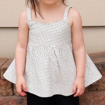 Toddler wearing a handmade white tank top with black polka dots, featuring a flared gathered waist and wide shoulder straps.